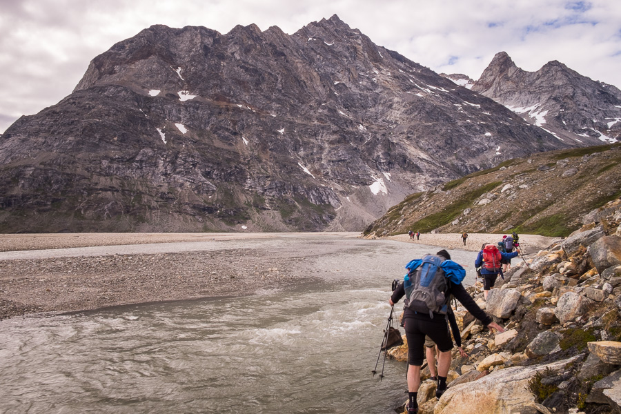 Trekking group picking their way along the rocks lining the river to avoid the water for as long as possible