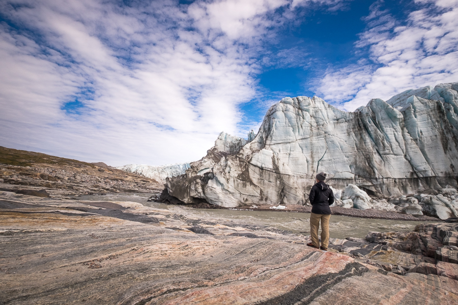 Me standing on rocks looking across the river at the 60m high face of the Russell Glacier