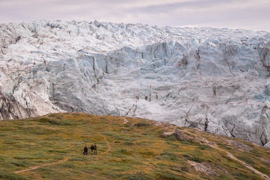 Three visitors hiking to the main viewpoint over the Russell Glacier with the sheer wall of the glacier in front of them. Near Kangerlussuaq, West Greenland
