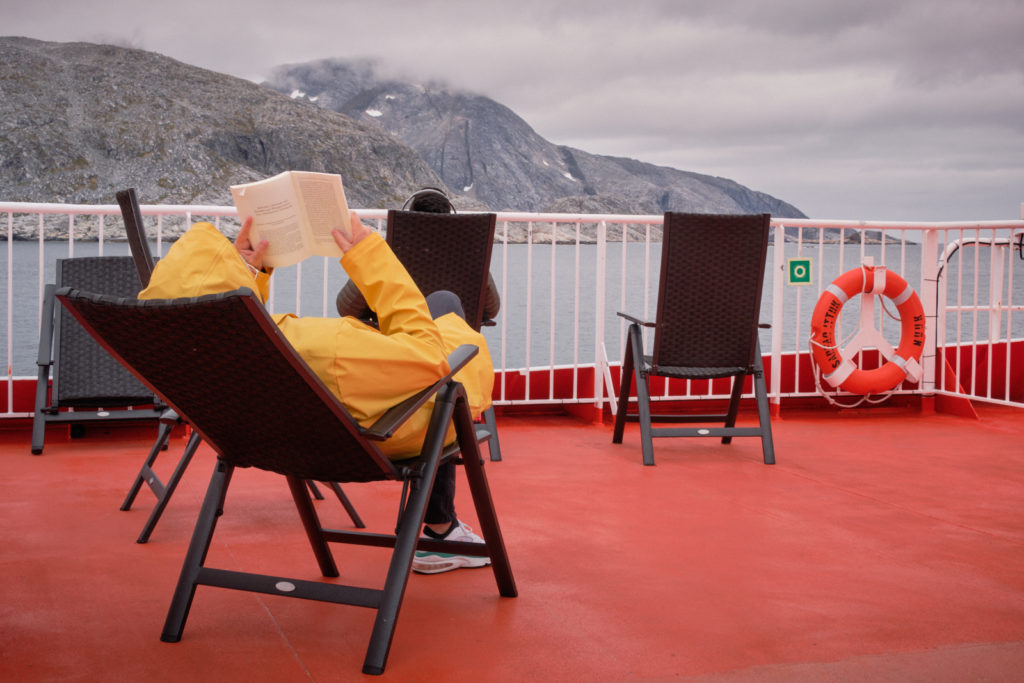 Person reading a book on the top deck of Sarfaq Ittuk, rugged up against the cold
