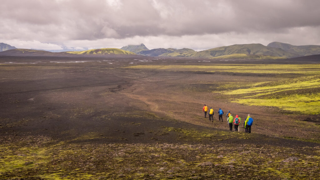 Guided hikers moving through volcanic terrain on a multi-day hiking route in Iceland.