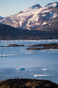 Distant view of 2 people sitting on a hill overlooking the Tasiilaq fjord watching the sunset - East Greenland