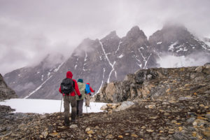 My trekking companions in full rain gear hiking through more snow with mountains in the background