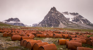 Hundreds of rusted fuel barrels in front of the mountains of East Greenland