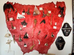 Large red leather hide hanging on the wall with feet, bones, teeth and other animal parts attached to it, in the Kulusuk museum