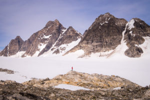 Our trekking guide at a distance standing on a small hill looking up at the mountains towering above him