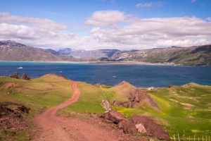 A red dirt road leads down green hills to the fjord and Qassiarsuk, South Greenland