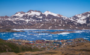 Looking down on the colourful buildings of Tasiilaq from a high vantage point, with the Tasiilaq Fjord and mountains in the background. East Greenland