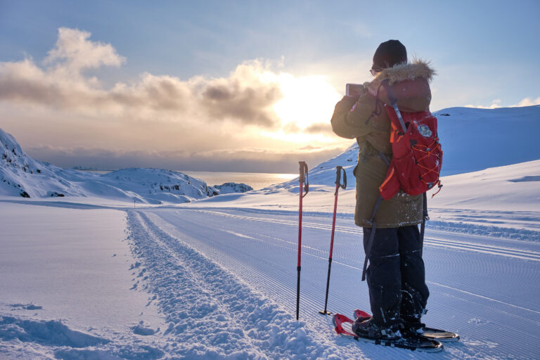 hiker taking photograph of the ocean on a snowshoeing trip near sisimiut